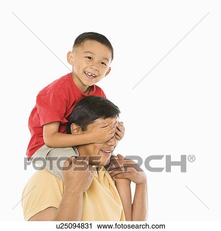 Stock Image - Asian boy sitting on father's shoulders with hands over his eyes in front of white background.. Fotosearch