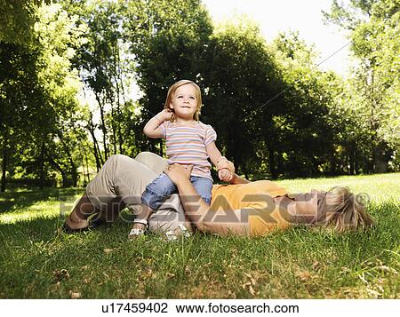 Caucasian mid adult woman lying in grass at park with toddler daughter seated on her lap. View Large Photo Image Stock Image - Caucasian mid adult woman lying in grass at park with toddler daughter seated on her lap.. Fotosearch