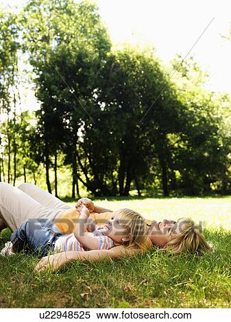 Stock Photography - Caucasian mid adult woman with toddler daughter lying in grass at park relaxing.. Fotosearch