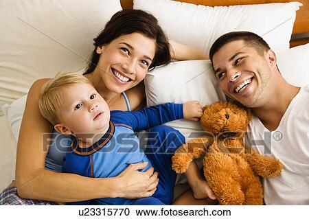 Stock Image - Caucasian parents and toddler son lying in bed smiling.. Fotosearch