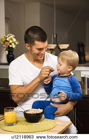 Man feeding toddler son on lap in kitchen View Large Photo Image Stock Image - Man feeding toddler son on lap in kitchen . Fotosearch