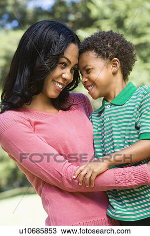 Stock Image - Mother and son with arms around eachother looking at eachother and smiling.. Fotosearch