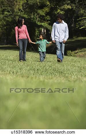 Stock Photograph - Parents and young son walking in park holding hands.. Fotosearch