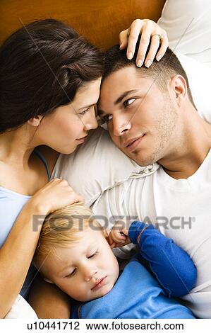 Stock Image - Parents cuddling with toddler son in bed.. Fotosearch