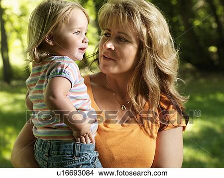 Picture - Woman holding toddler in arms at park. Fotosearch