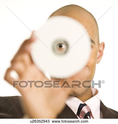 Stock Image - African American man holding compact disc over face and peeking through hole.. Fotosearch