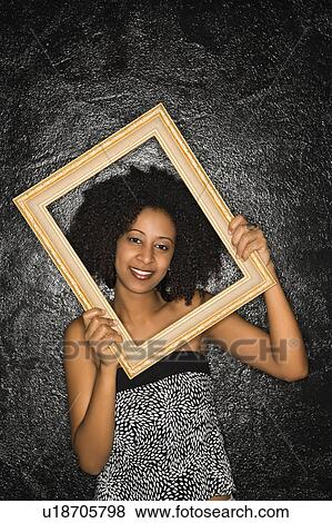 Stock Photo - African-American woman holding frame over her face.. Fotosearch