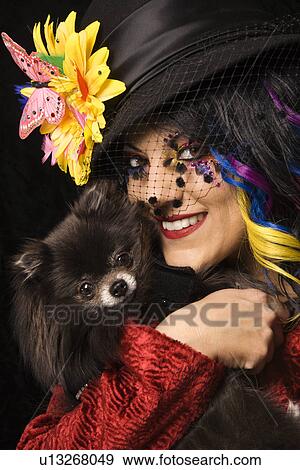 Stock Photo - Caucasian adult in unique makeup and clothing holding black Pomeranian dog.. Fotosearch