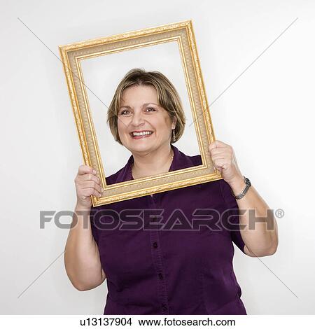 Picture - Caucasian middle aged woman holding picture frame over face.. Fotosearch