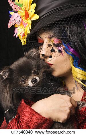 Stock Image - Caucasian woman in unique makeup and clothing holding and kissing black Pomeranian dog.. Fotosearch