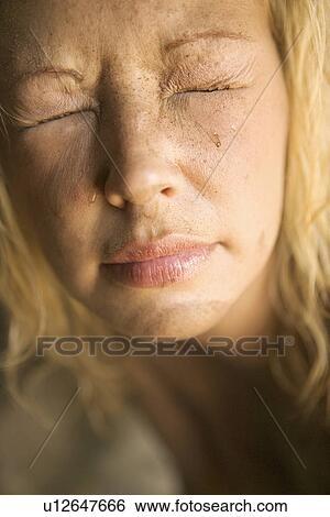 Stock Photograph - Close-up of blond womans muddy face with closed squinting eyes.. Fotosearch