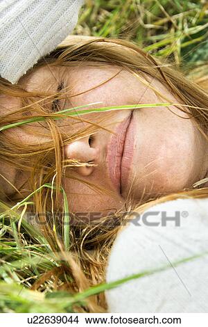 Picture - Close up portrait of attractive young redheaded woman lying in grass resting.. Fotosearch