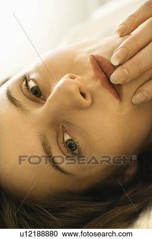 Stock Image - Close up portrait of Caucasian mid-adult woman looking at viewer touching fingers to lips.. Fotosearch