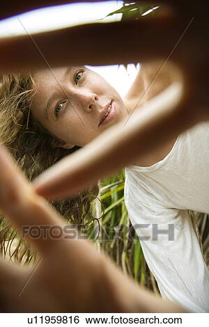 Stock Photograph - Low angle view of Caucasian young adult woman holding hands out to camera and peeking through fingers.. Fotosearch