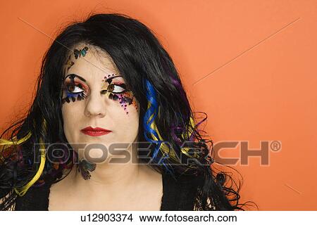 Picture - Portrait of Caucasian woman with unique makeup and hair against orange background.. Fotosearch