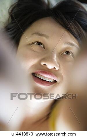 Stock Image - Portrait of pretty young Asian woman lying in bed smiling.. Fotosearch