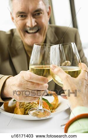 Stock Image - Caucasian mature couple toasting with white wine in restaurant.. Fotosearch