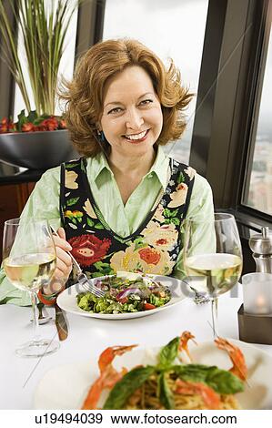 Stock Photo - Caucasian mature woman with meal in restaurant smiling.. Fotosearch