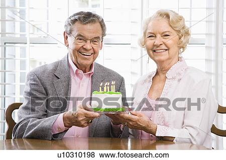 Stock Photo - Couple holding birthday cake looking at viewer.. Fotosearch