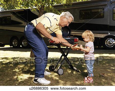 Stock Photography - Grandfather giving granddaughter hotdog by RV.. Fotosearch