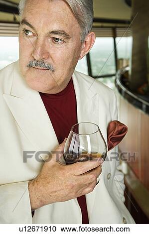 Stock Image - Man in suit holding snifter of brandy. Fotosearch