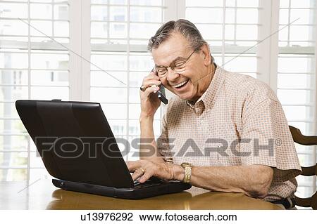 Man typing on laptop and talking on cellphone View Large Photo Image Stock Image - Man typing on laptop and talking on cellphone. Fotosearch
