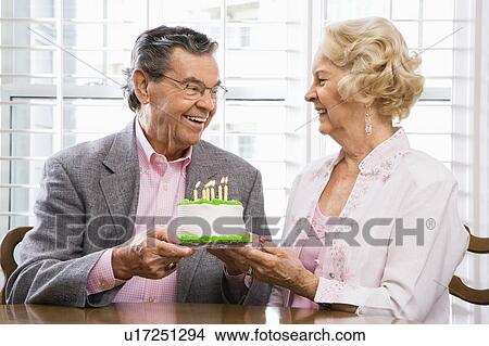 Picture - Mature Caucasian couple holding birthday cake looking at each other.. Fotosearch