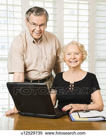 Stock Photography - Mature Caucasian couple looking at their calendar and using laptop.. Fotosearch