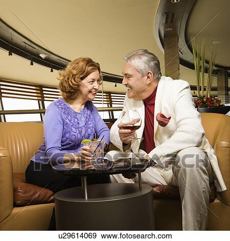 Stock Photo - Mature Caucasian couple sitting in bar lounge having drinks and talking.. Fotosearch