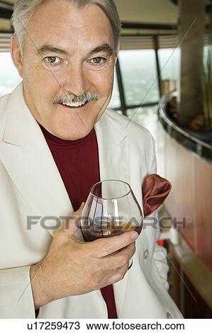 Stock Image - Mature Caucasian man in suit holding snifter of brandy smiling.. Fotosearch
