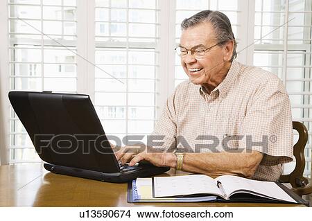 Picture - Mature Caucasian man typing on laptop in home.. Fotosearch