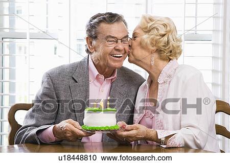 Stock Image - Mature Caucasian woman kissing mature Caucasian man while holding birthday cake.. Fotosearch