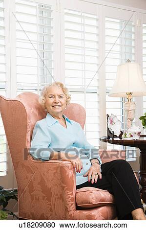 Stock Image - Mature Caucasian woman sitting in chair looking at viewer.. Fotosearch