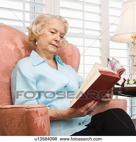 Stock Photo - Mature Caucasian woman sitting in chair reading a book.. Fotosearch