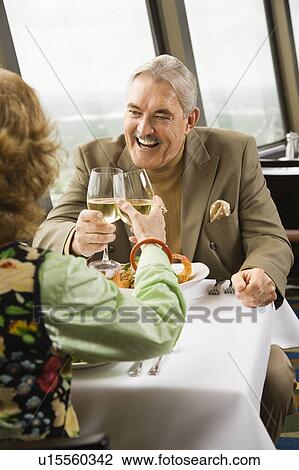 Mature couple dining and toasting in fancy restaurant by window with rooftop view of urban landscape. View Large Photo Image Stock Image - Mature couple dining and toasting in fancy restaurant by window with rooftop view of urban landscape.. Fotosearch