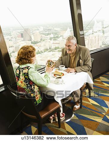 Stock Image - Senior couple having dinner in nice restaurant as man gives gift to woman. Fotosearch