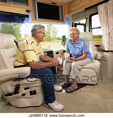 Stock Photo - Senior couple sitting in RV holding coffee cups and smiling. Fotosearch