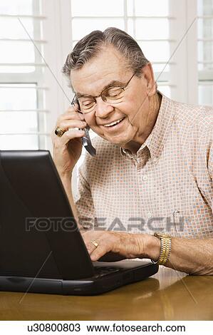 Senior man typing on laptop and talking on cellphone View Large Photo Image Stock Image - Senior man typing on laptop and talking on cellphone. Fotosearch