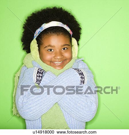 Stock Image - African American girl in winter clothing with arms crossed smiling at viewer.. Fotosearch