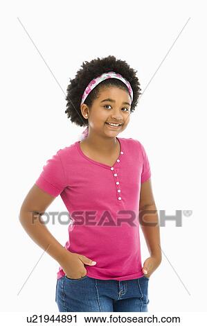 Stock Image - African American girl with hands in pockets wearing headband smiling at viewer.. Fotosearch