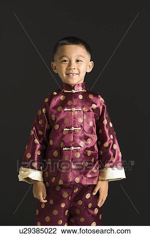 Stock Image - Asian boy in traditional attire standing against black background.. Fotosearch