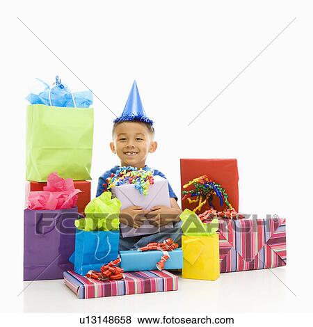 Stock Photo - Asian boy sitting smiling wearing party hat with wrapped presents.. Fotosearch