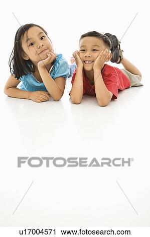 Stock Image - Asian brother and sister lying on floor with heads on hands.. Fotosearch