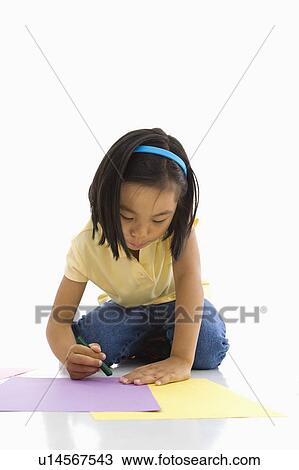 Stock Image - Asian girl sitting on floor coloring on paper.. Fotosearch