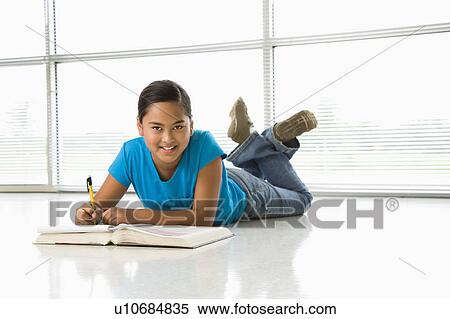 Stock Photography - Asian preteen girl lying on floor doing homework looking up at viewer.. Fotosearch