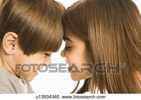 Stock Image - Boy and girl with heads together making mean faces.. Fotosearch