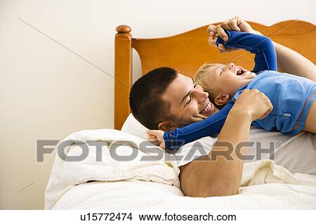 Caucasian toddler boy and father playing and tickling in bed. View Large Photo Image Picture - Caucasian toddler boy and father playing and tickling in bed.. Fotosearch