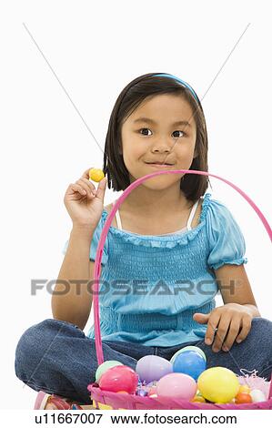 Stock Photo - Girl sitting on floor with Easter basket full of eggs smiling. Fotosearch