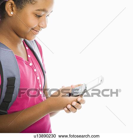 Stock Image - Girl with backpack text messaging on cell phone. Fotosearch
