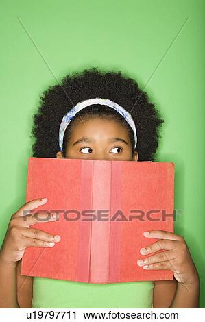 Stock Image - Girl with book held up to face looking suspiciously to the side. Fotosearch